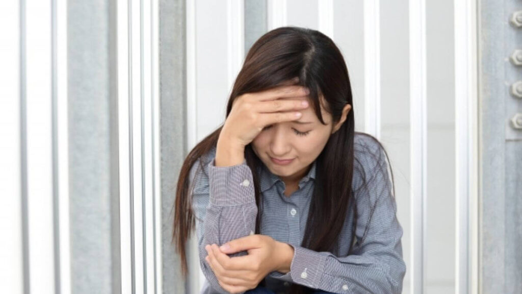 頭を抑えながら座る髪の長い女性