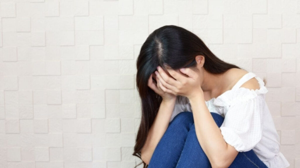 床に座ってうずくまりながら落ち込む女性