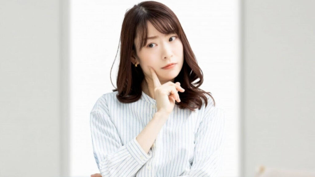 指を頬に当て考え事をする若い女性