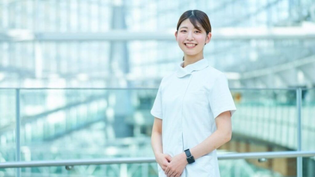 病院の廊下で微笑む若い白衣の女性