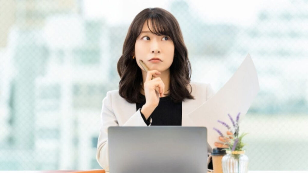 パソコンで仕事をしながら疑問を持つスーツ姿の女性