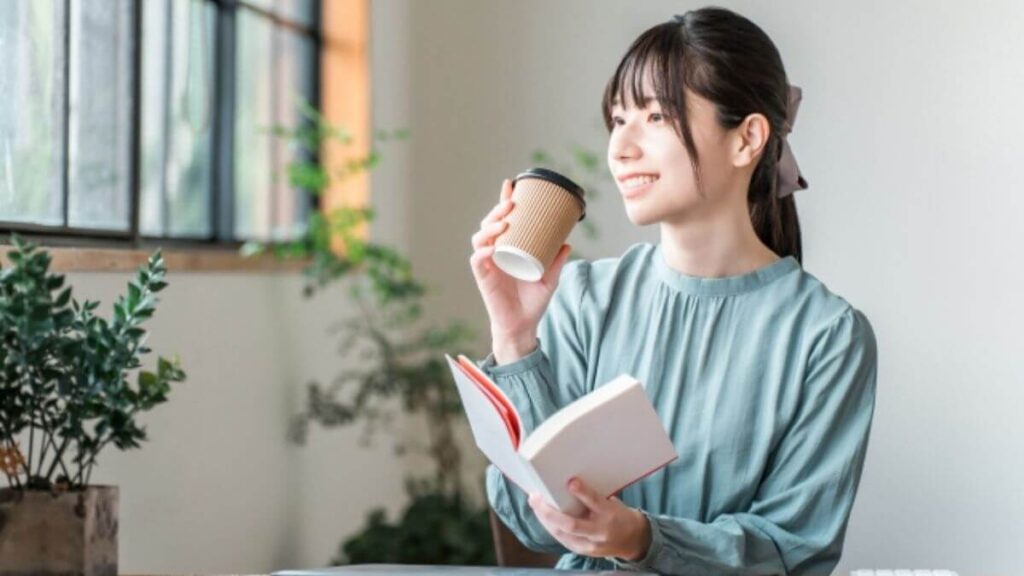 コーヒーを片手に本を読む若い女性