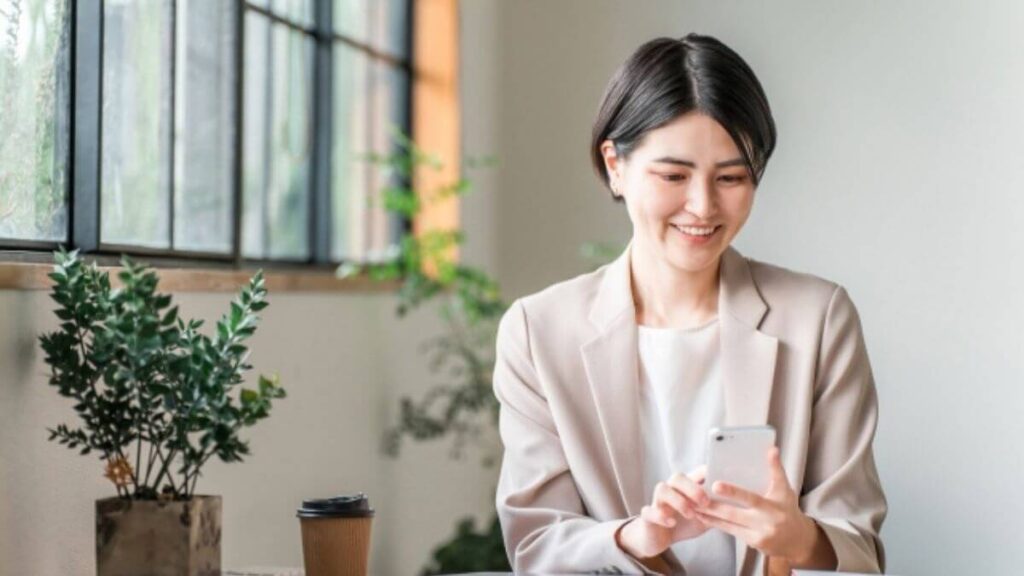 笑顔でスマートフォンを触るスーツ姿の女性