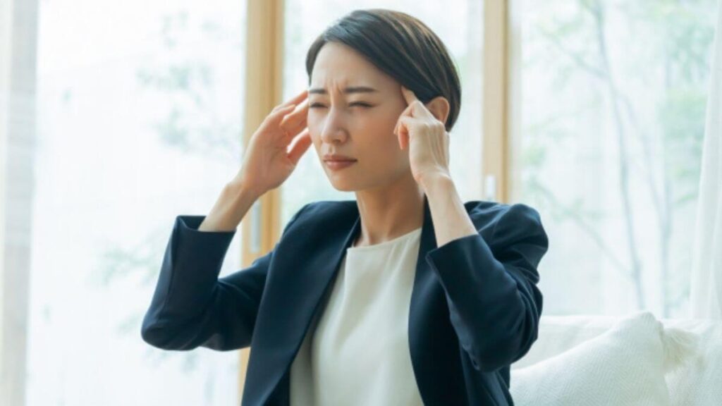 頭を抱え体調が悪そうなスーツ姿の女性