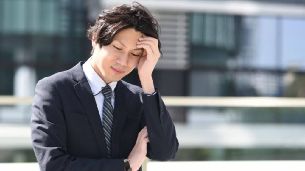 手を顔に当て悩んだ表情をするスーツ姿の男性