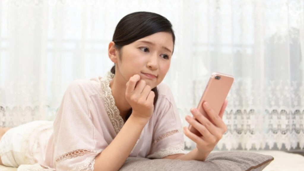 スマートフォンを見ながら悩む主婦
