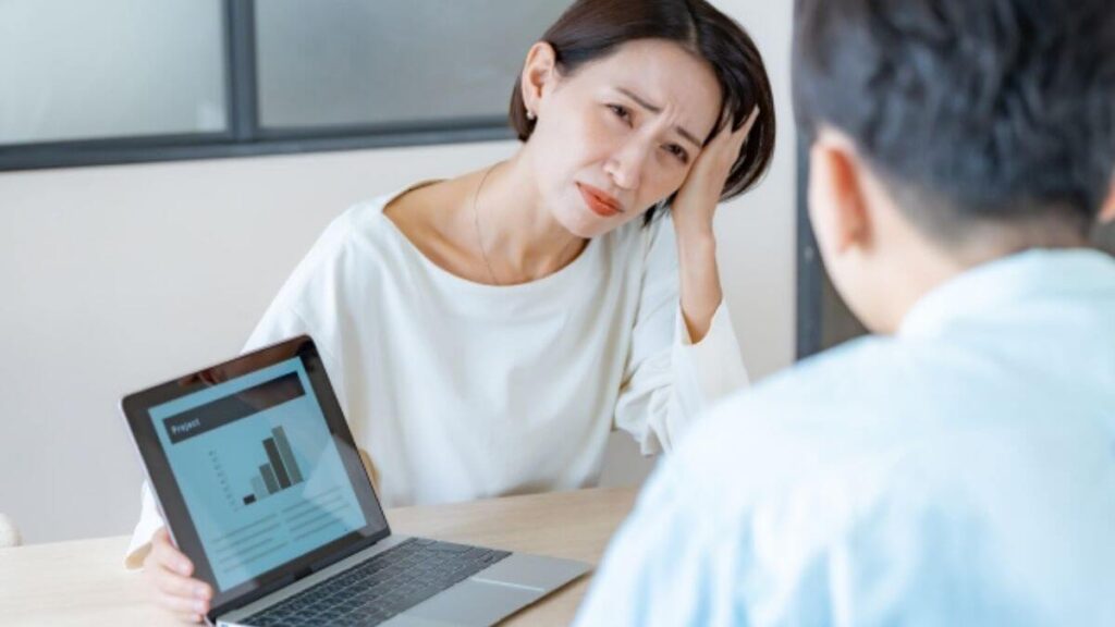 同僚との会議中につらそうな表情をする女性