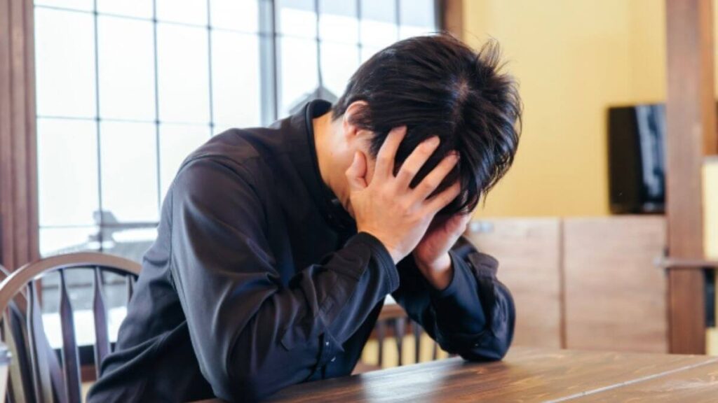 机の上でうなだれて落ち込む男性