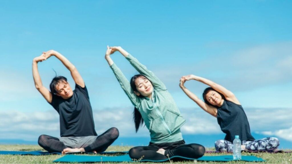 青空の下でヨガをする男女3人