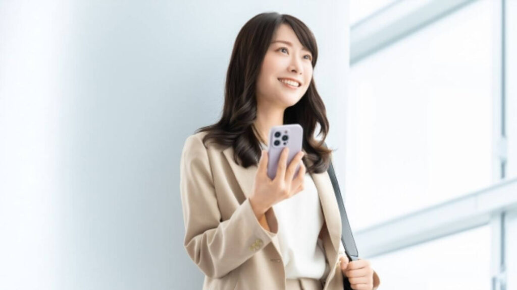 スマホを持ち明るい表情で歩くスーツ姿の女性