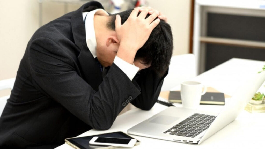 自分の机で頭を抱えるスーツ姿の男性