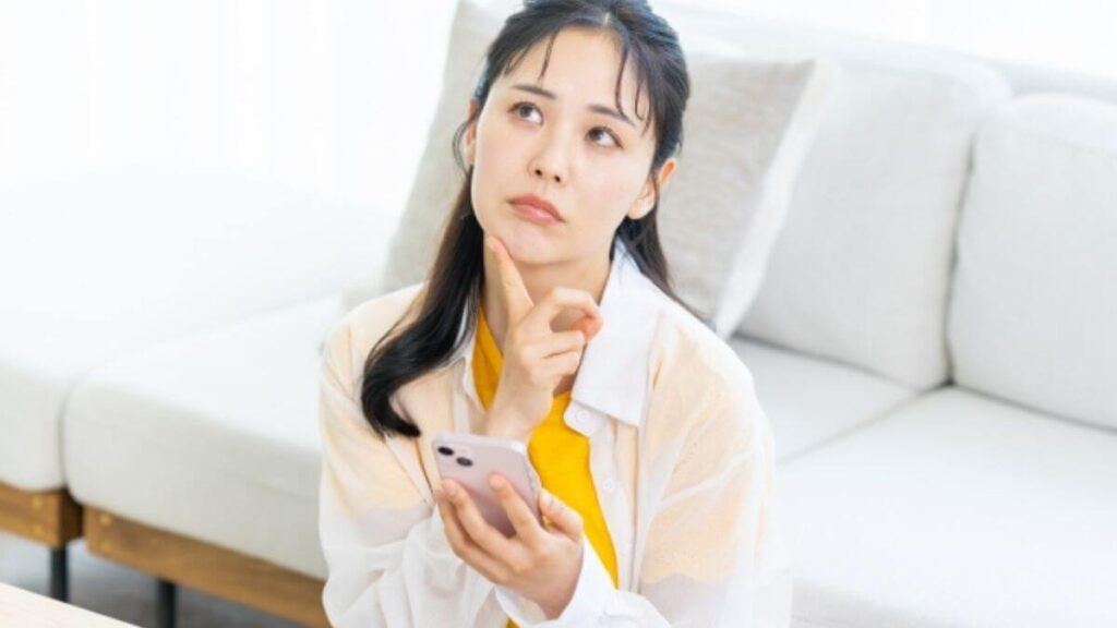 スマホを持ちながら顎に指を置き考える若い女性