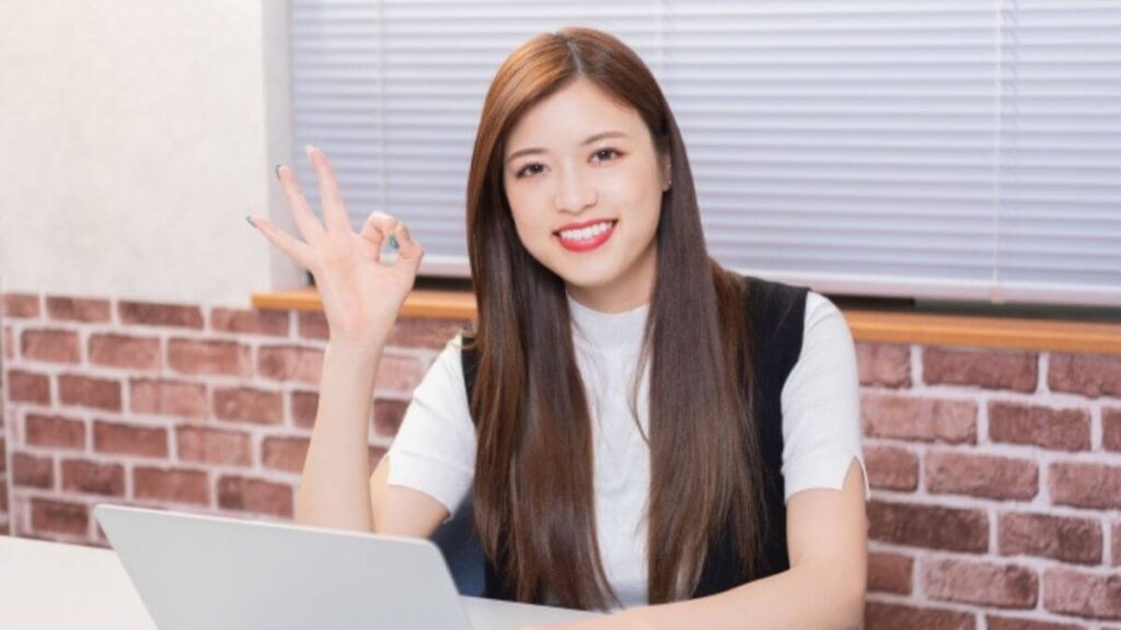 パソコンの前で笑顔でOKサインを出す若い女性