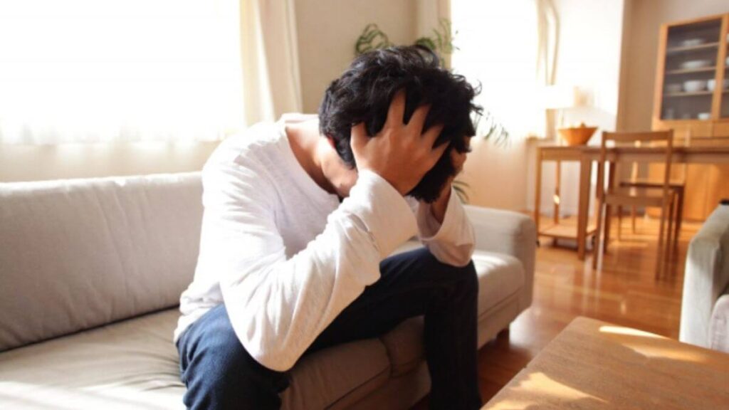 部屋で頭を抱え悩みこむ男性