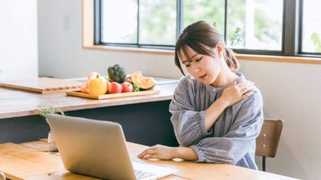 パソコン仕事をしながら肩を抑える若い女性