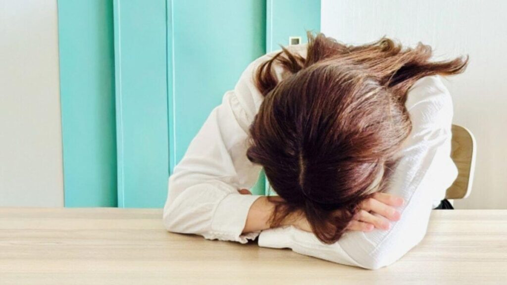 机の上に突っ伏し悩んでいる若い女性