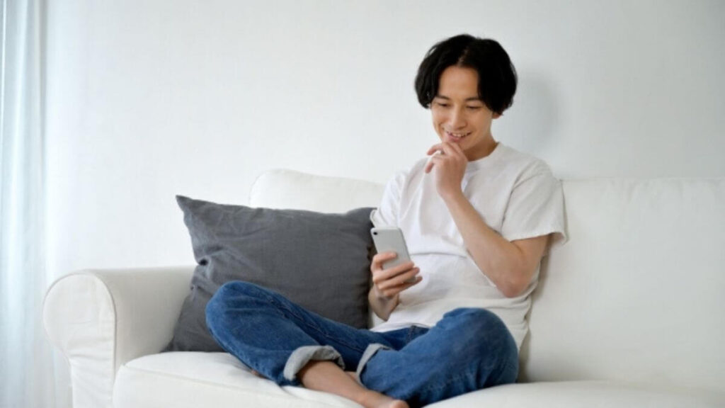 ソファーに座りながら笑顔でスマホを触る男性