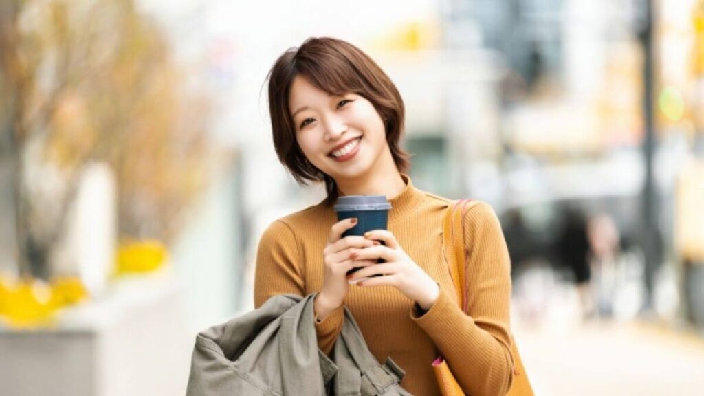 コーヒーを持ち笑顔で歩く若い女性